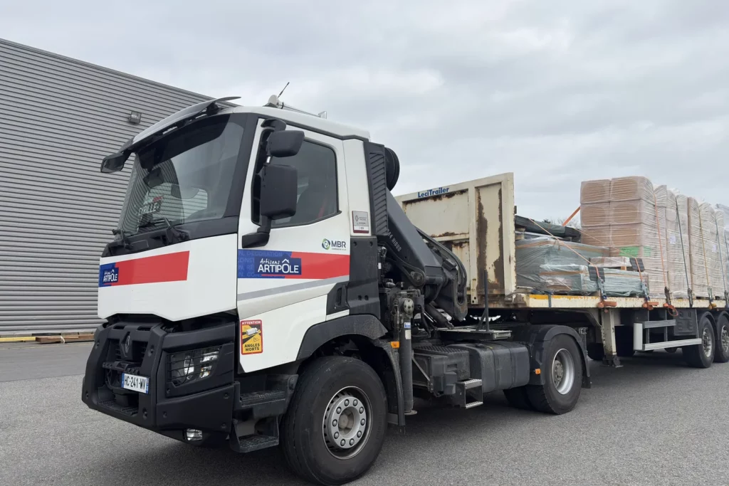 Camion plateau équipé d’une grue de manutention, chargé de matériaux